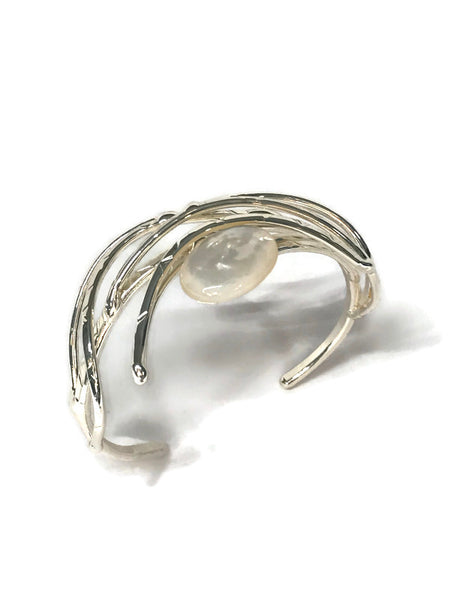 bracelet en laiton argenté, courbes de métal enserrant une nacre véritable, sur environ 2,5 cm de large, vue de dessus