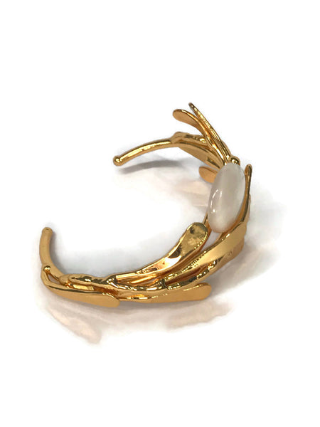 bracelet de créateur, doré, motif végétal, petites feuilles assemblées qui capte la lumière, cabochon de nacre au centre,vue de biais