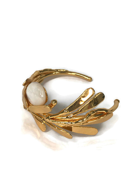 bracelet de créateur, doré, motif végétal, petites feuilles assemblées qui capte la lumière, cabochon de nacre au centre,vue de biais