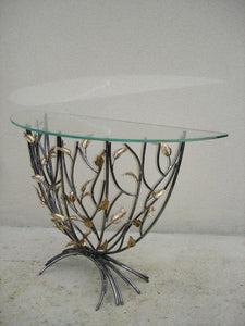 console en forme de demi-lune, plateau de verre porté par un entrelacs de tiges d'acier ornées de feuilles en laiton, vue de biais