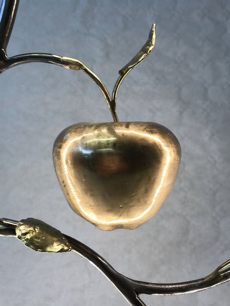 lampe à poser composée d'un cercle d'acier dans lequel un branchage avec feuilles de laiton abrite une pomme martenée en volume ; la pomme est en laiton ; un ruban led fait le pourtour du cercle d'acier ; zoom sur la pomme